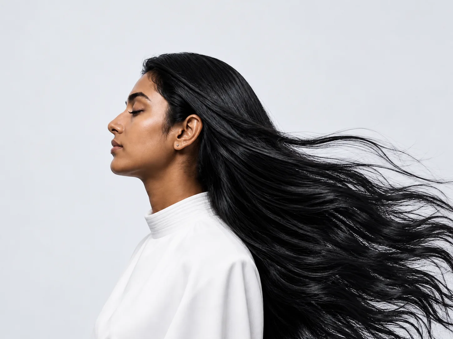 woman in profile with long black hair flowing to the right, wearing a white blouse.